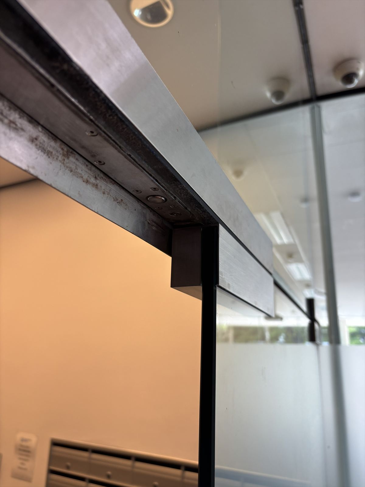 The finished CNC-machined metal fitting installed along the top of a glass door frame